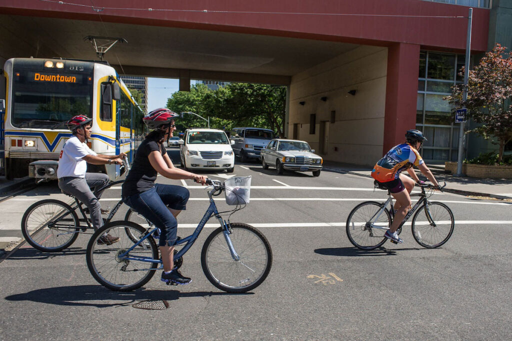 Cyclists crossing the street while a train and cars yield