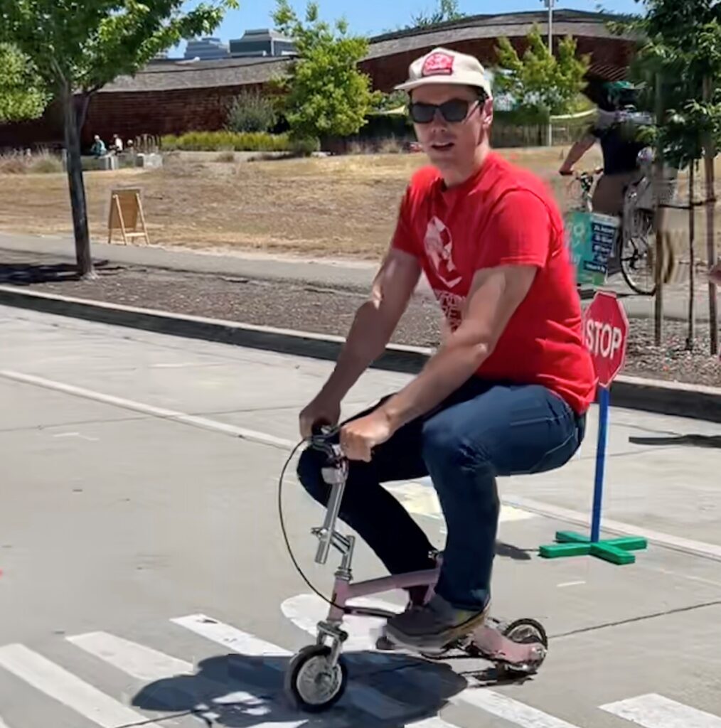 man wearing a red shirt, hat, and sunglasses riding a small bike