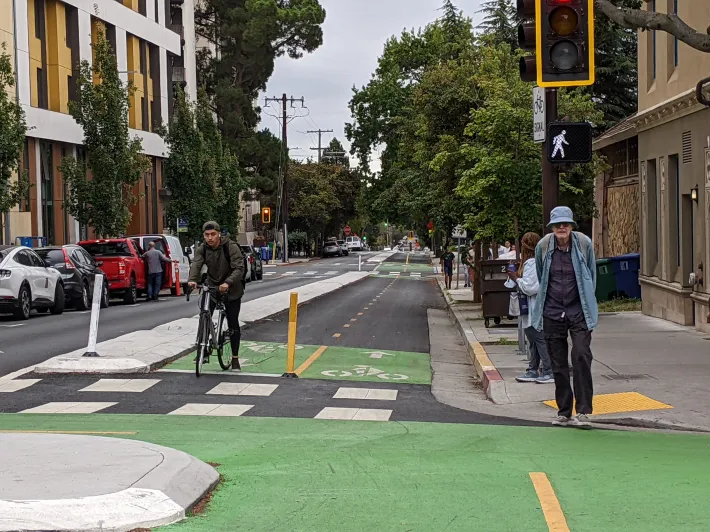 Person riding a bike in a separated bikeway and an older adult walking into an intersection.