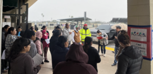 Photo of a group of people gathered around listening to one man speak.