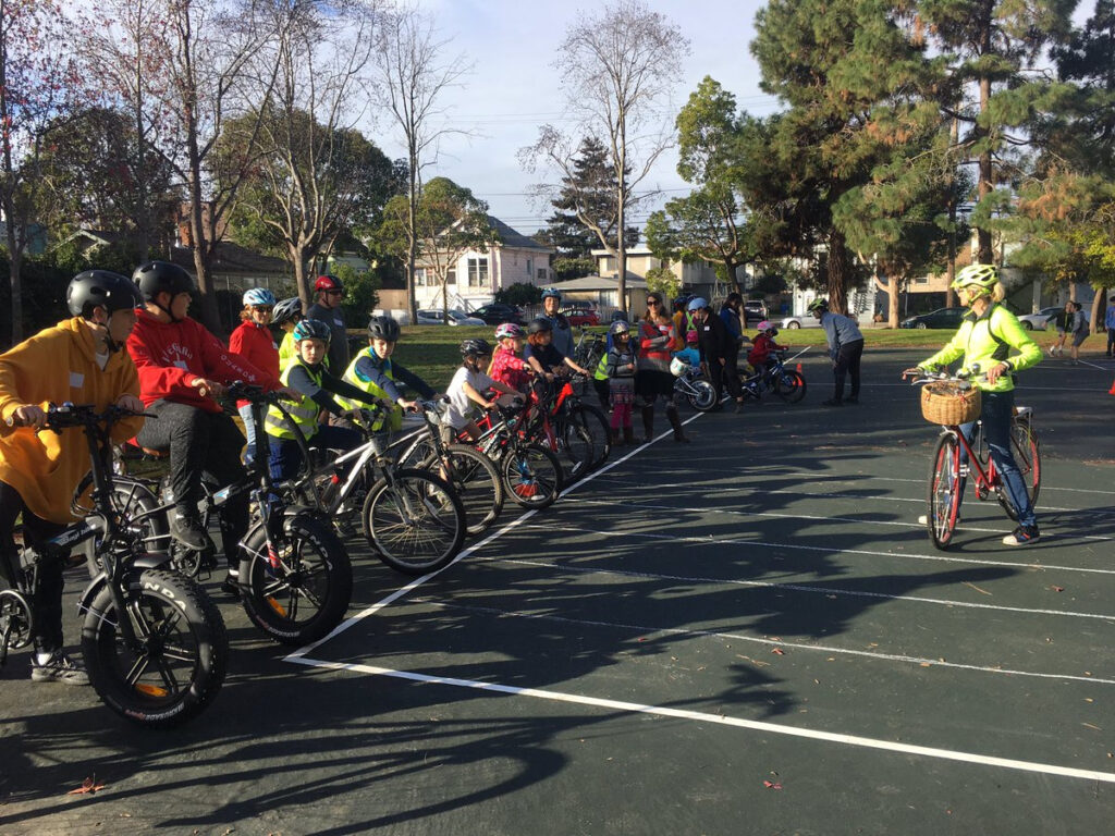 Group of bicyclists lined up on blacktop facing bicycling instructor